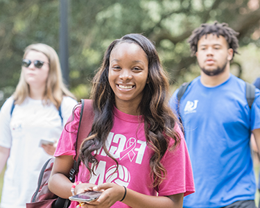Student smiling walking outside on campus holding her cell phone.